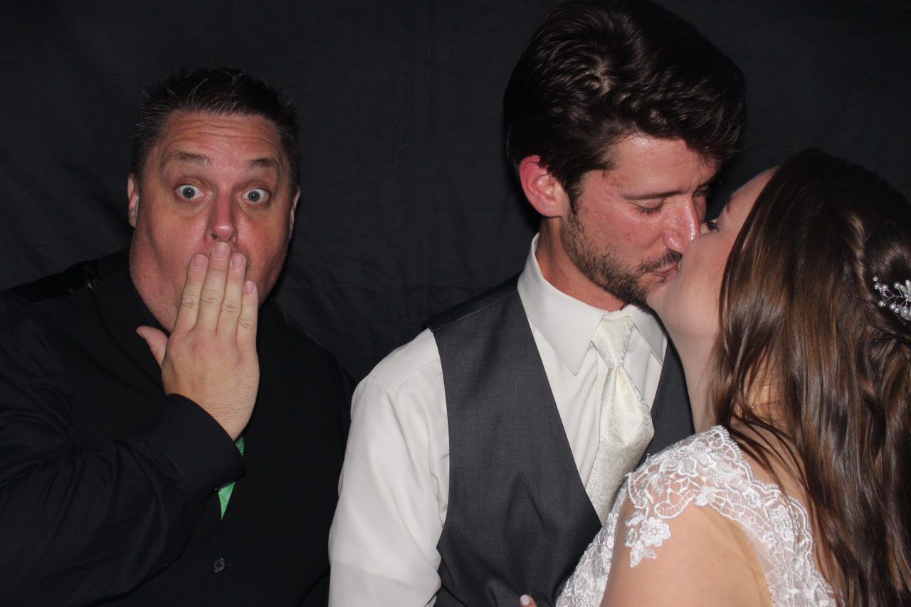 A surprised man reacts as a couple shares a kiss at a wedding.